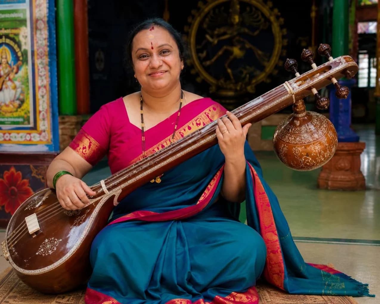 Chandana Nerella smiling, seated with a tambura in a temple hall